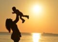 Silhouette of a mother lifting her child at a sunset beach, capturing warmth and love.