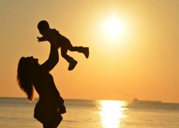 Silhouette of a mother lifting her child at a sunset beach, capturing warmth and love.