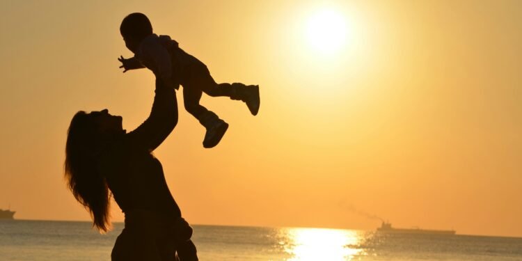 Silhouette of a mother lifting her child at a sunset beach, capturing warmth and love.