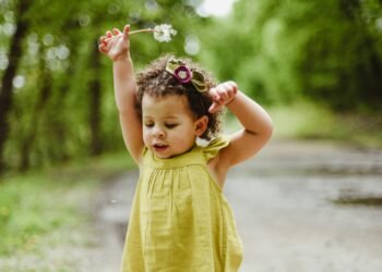 Adorable young girl playing in a lush green forest on a bright spring day.