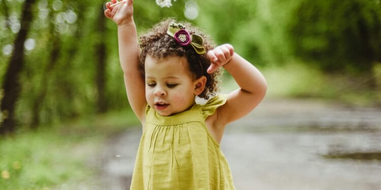 Adorable young girl playing in a lush green forest on a bright spring day.