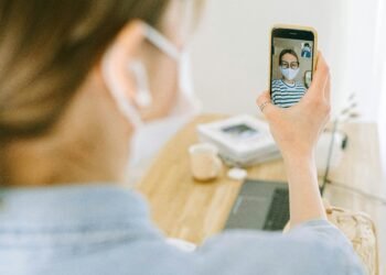 Woman wearing face mask making a video call on smartphone in cozy home setting.