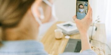 Woman wearing face mask making a video call on smartphone in cozy home setting.